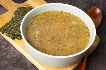 Vegan seaweed and tofu soup in a bowl on a serving board. Pieces of nori seaweed and a spoon on the board next to the bowl