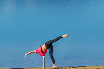 7 years old girl with pink shirt and sportswear doing a cartwheel at the beach during spring with blue water as background. Palencia, Spain