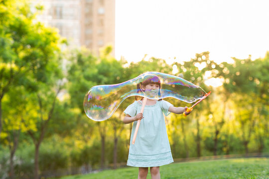Happy little girl blowing bubbles on grass