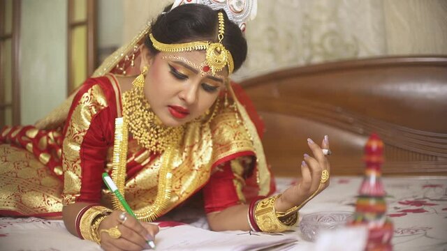 Sad young Indian bride smoking cigarette and writing suicide note at home before arranged marriage, golden jewellery
