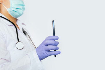 Woman with a medical mask and stethoscope around her neck holding a smartphone.