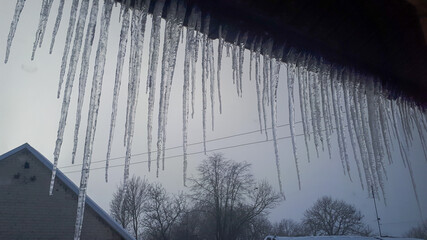spring landscape with ice icicles hanging from roof of house concept