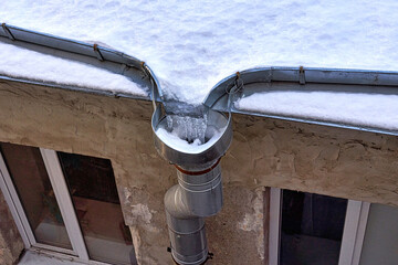 Fragment of the snow-covered roof of an old house with a drain with frozen water - 427206163
