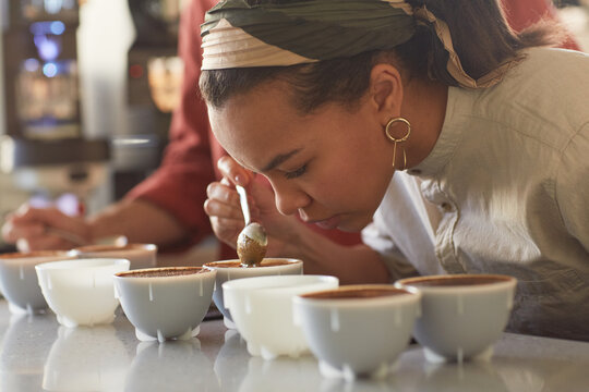 Side view portrait of mixed race young woman smelling cofeee during quality assesment and cupping test in cafe, copy space