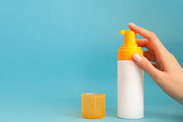 White and yellow sunscreen bottle with cream or lotion on the aqua blue background with female hand and copy space. Empty bottle mockup. Spf sun protection, summer skin care