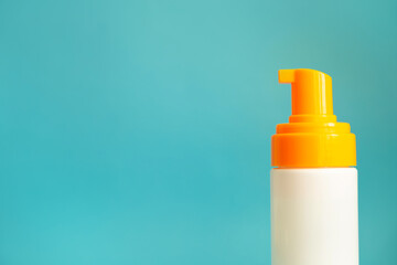 White and yellow sunscreen bottle with cream or lotion on the aqua blue background with copy space. Empty bottle mockup closeup