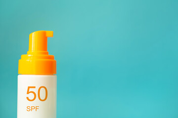 White and yellow sunscreen bottle with spf 50 cream or lotion on the aqua blue background with copy space closeup