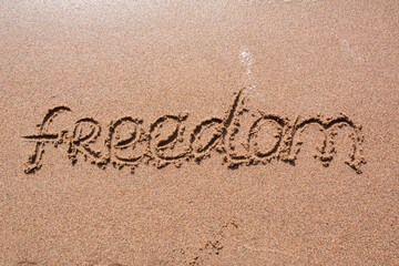 Fototapeta premium Word Freedom handwritten on a sandy beach