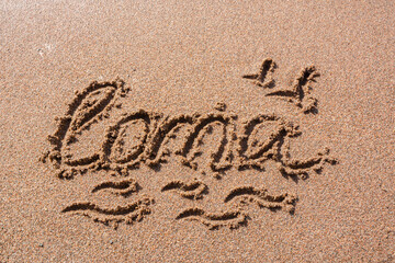 Fototapeta premium Finnish word Loma (vacation) handwritten on a sandy beach