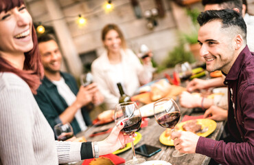 Happy couple toasting red wine with friends at rooftop party - Young man drinking with beautiful woman - Friendship concept with milenials having fun together - Warm bright filter with focus on glass