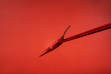 Red Chinese chopsticks derazht a small red hot chili pepper. Red on red. Ingredients for Asian food. Spicy food. Red background. Asian products. Macro photography of food.