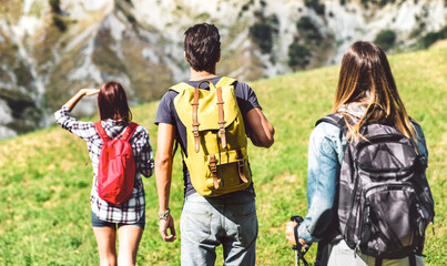 Friends group trekking on italian alps at afternoon - Hikers walking on mountain place - Wanderlust travel concept with young people at excursion in wild nature - Focus on central yellow backpack