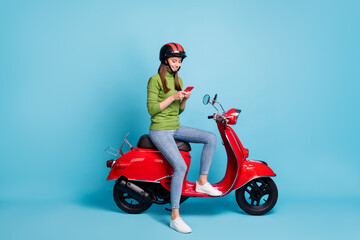 Obraz na płótnie Canvas Full length photo portrait of woman holding phone in two hands sitting on red scooter isolated on pastel blue colored background