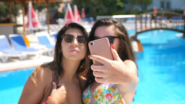 Attractive brunettes taking selfie portrait on smartphone. Young carefree women making photo during summer vacation. Beautiful ladies in sunglasses posing on camera. Two girlfriends resting together