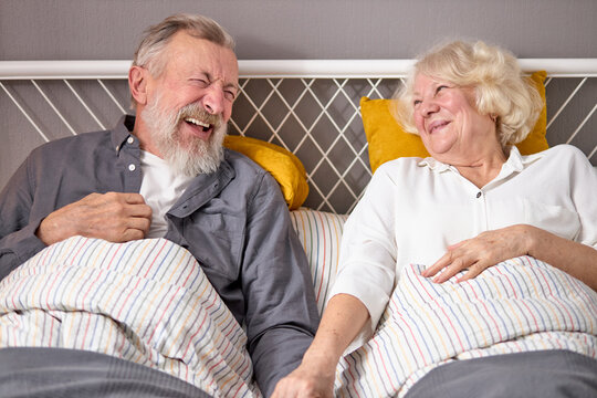 positive caucasian elderly couple have fun. laugh while lying on bed at home