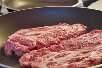 Salted red pork steaks in a frying pan.