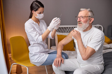 Female Doctor Preparing Syringe For Making Injection To Elderly Man