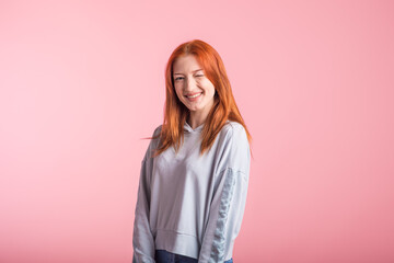 Redhead girl winks in studio on pink background
