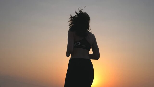 Active slim girl jogging on country road with evening sky at background. Unrecognizable female sportsman doing run training. Young sporty woman working out outdoor at sunset. Healthy lifestyle.