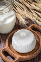 Round cottage cheese with milk and spikelets of wheat on background on a wooden table.