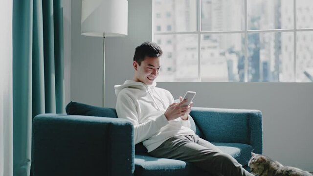 Smiling guy in white hoodie pets cat and films with phone