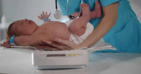 Cropped shot of nurse weighting on scales newborn baby