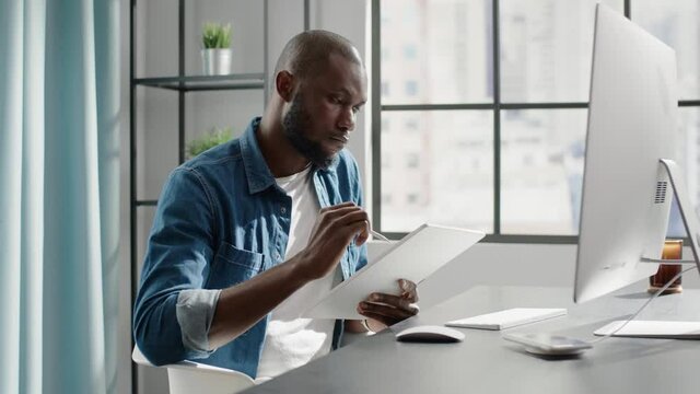 Black worker makes notes on project template on tablet