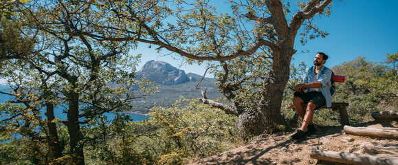 A man - a tourist with a backpack is resting on a bench in the mountains.