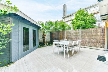 Modern table with chairs located on tiled floor near thatch fence in backyard of blue house