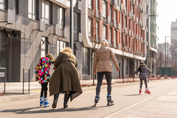 A happy family in roller skates, grandma teaches two granddaughters to roller-skate