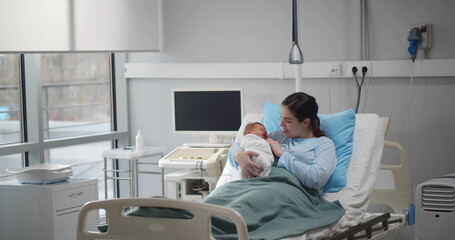 Young mother with newborn baby resting in hospital bed