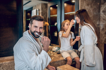 Cute family in bath robes brushing teeth together