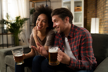 Boyfriend and girlfriend drinking beer at home. Happy couple watching sports game on tv...