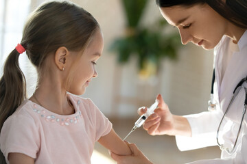 Close up of young Caucasian female nurse vaccinate small girl child at checkup in hospital. Woman...