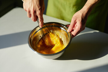 Tasty homemade cakes baking, Easter pie preparing or cookie concept. Chef in green apron mixing sugar and eggs in a stainless steel bowl using wire whisk. High quality photo
