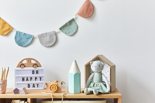 Stylish scandinavian newborn baby room with toys, plush animal, photo camera, dolls and child accessories. Cozy decoration and hanging cotton balls on the white wall. Copy space.