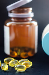 Yellow medicine pills in close-up on a black backdrop with their container in the background.