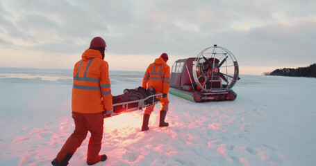 Rescue service team loading victim on stretcher in air-boat patrolling coast in winter