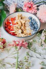 Trendy breakfast bowl of nuts, cereal, berries and yogurt with colorful floral frame. Healthy muesli with fresh fruits. Food styling.