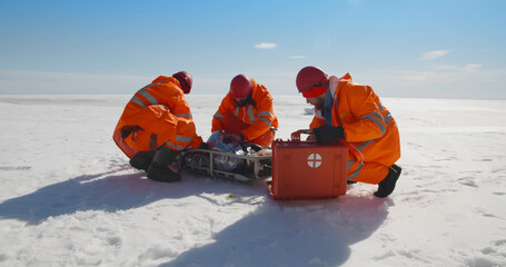 Lifeguard team providing first aid to unconscious person lying on stretcher in arctic
