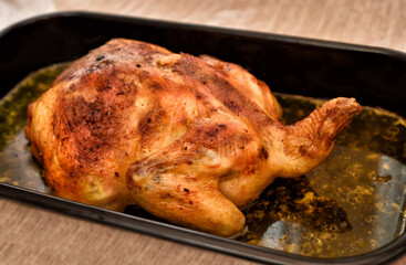 Roasted chicken in a black baking pan with too much oil. Very tasty but unhealthy, oily and fatty food. Selective focus.