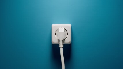 Plugged into an electrical outlet on a blue wall - obrazy, fototapety, plakaty