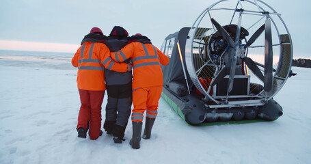 Lifeguards helping fisherman with injured leg getting in hovercraft in winter