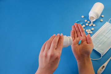 Medicine and healthcare concept. The woman removes the capsule from the container. Capsules, pills, medical mask on a blue background. Place for your text.