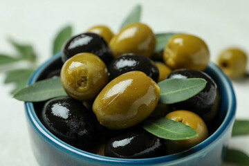 Bowl of olives and leaves on white background, close up