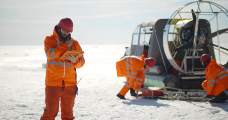 Coast guard team standing on frozen lake with hovercraft on background