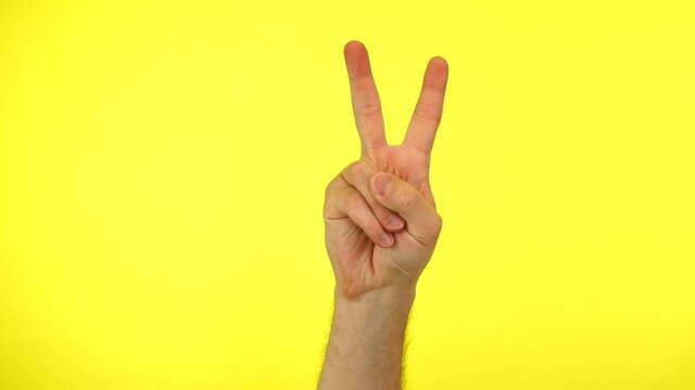 Man's hand showing victory or double on a yellow background.