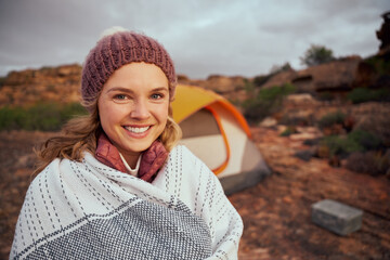 Smiling woman with blanket on mountain standing outside tent during camping at mountain hill