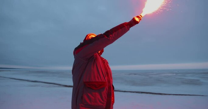 Man or fisherman firing red maritime distress signal flare on winter time