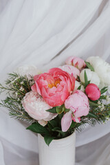 Stylish peonies bouquet on background of soft white fabric, flowers in ceramic vase. Mothers day